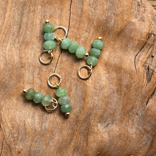 Three pairs of green beaded jewelry with gold-toned rings, arranged on a textured brown wood surface.